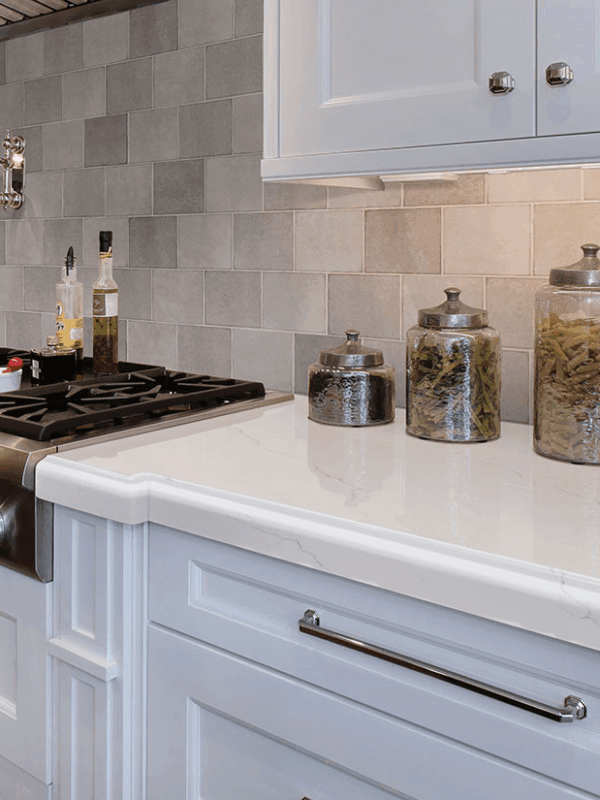Calacatta Miraggio quartz countertop in a white kitchen design with white cabinets and a tile backsplash.